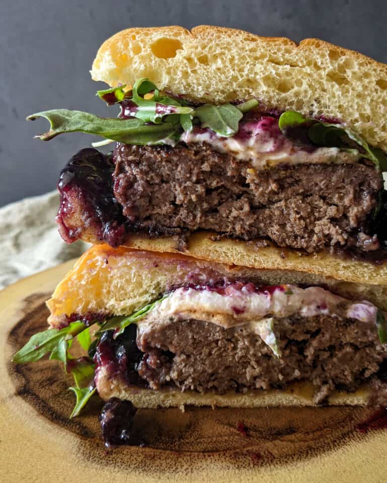 Two halves of a burger stacked to show layers of goat cheese, blueberry preserves, and arugula