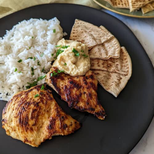 A plate of mediterranean marinated chicken and rice served with hummus and pita bread