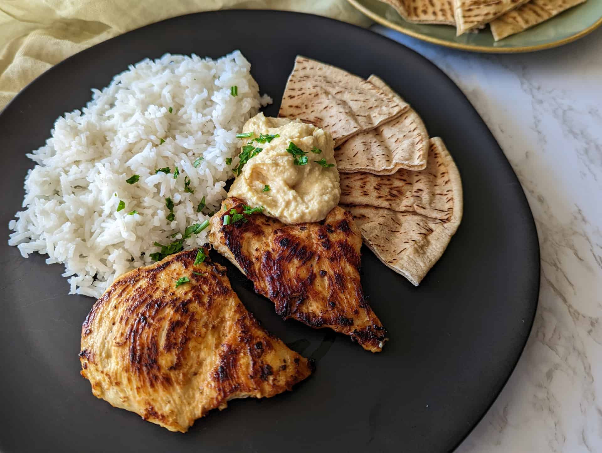 A plate of mediterranean marinated chicken and rice served with hummus and pita bread
