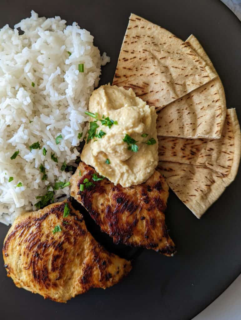 Mediterranean chicken and rice served with hummus and pita bread on a plate