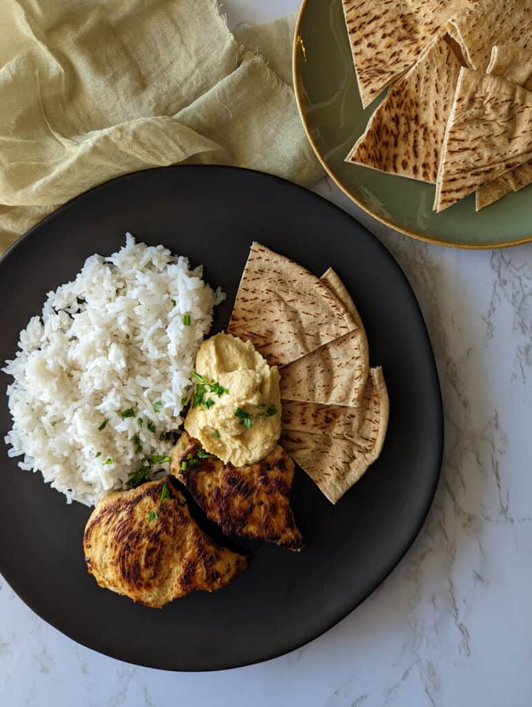 A plate of mediterranean marinated chicken, rice, and hummus served with pita bread