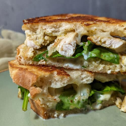 A pesto chicken and spinach panini stacked on a plate