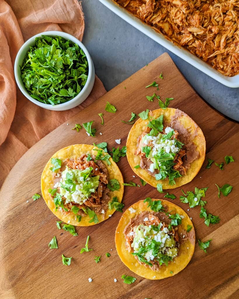 Chicken tinga tostada recipe on a plate with cilantro and shredded chicken tinga