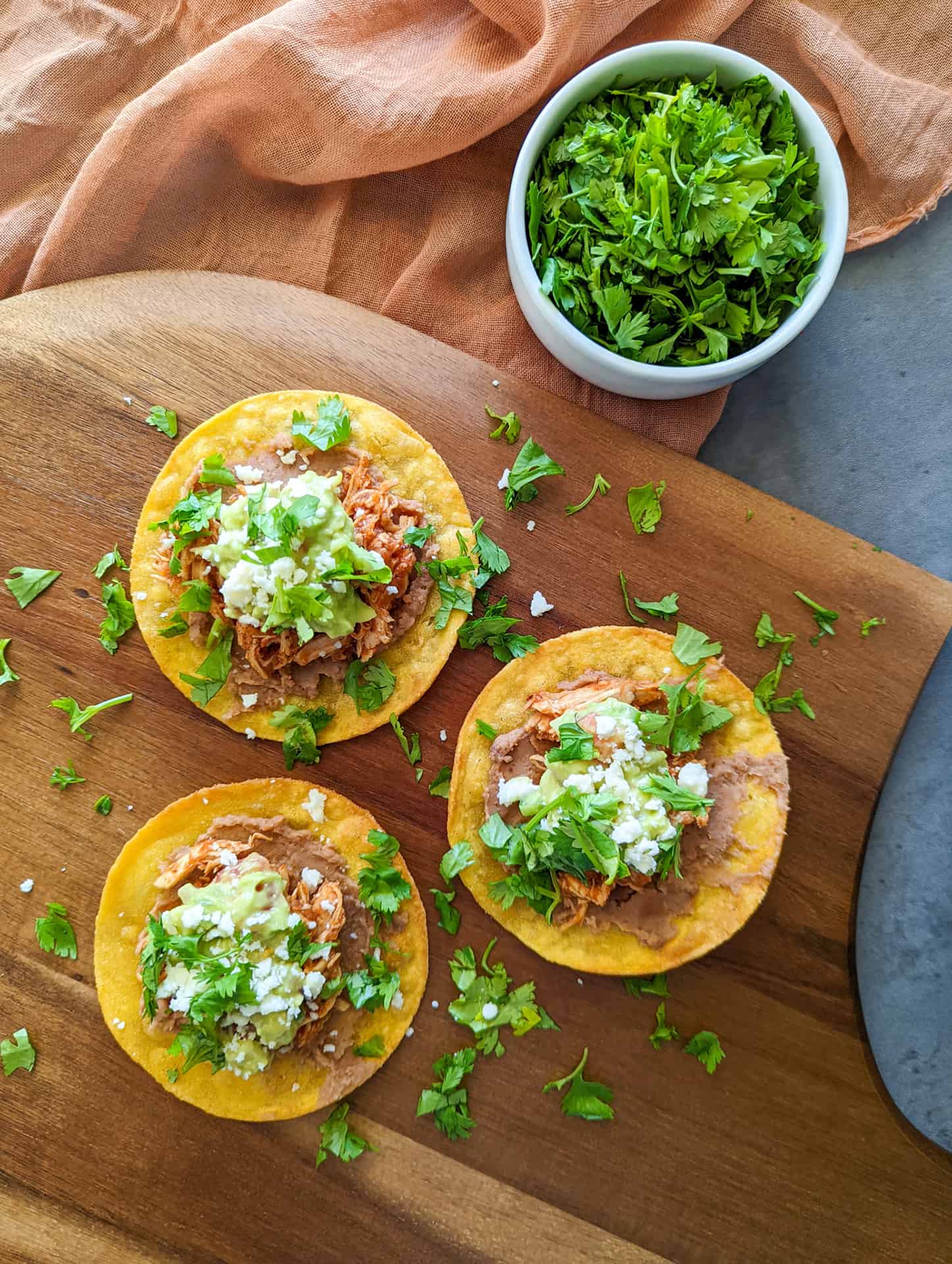 Authentic Mexican chicken tinga tostadas made with refried beans, mashed avocado, queso fresco, and chopped cilantro on a wooden pizza peel. 