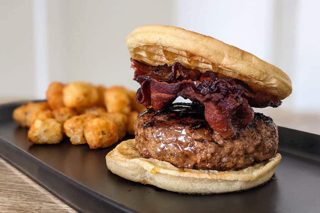 A maple bourbon burger with crispy bacon served between two waffles with a side of tater tots