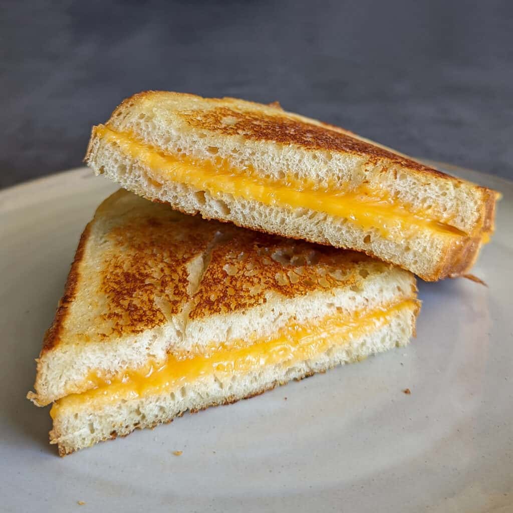 Two halves of a perfectly gooey grilled cheese sandwich stacked on a plate