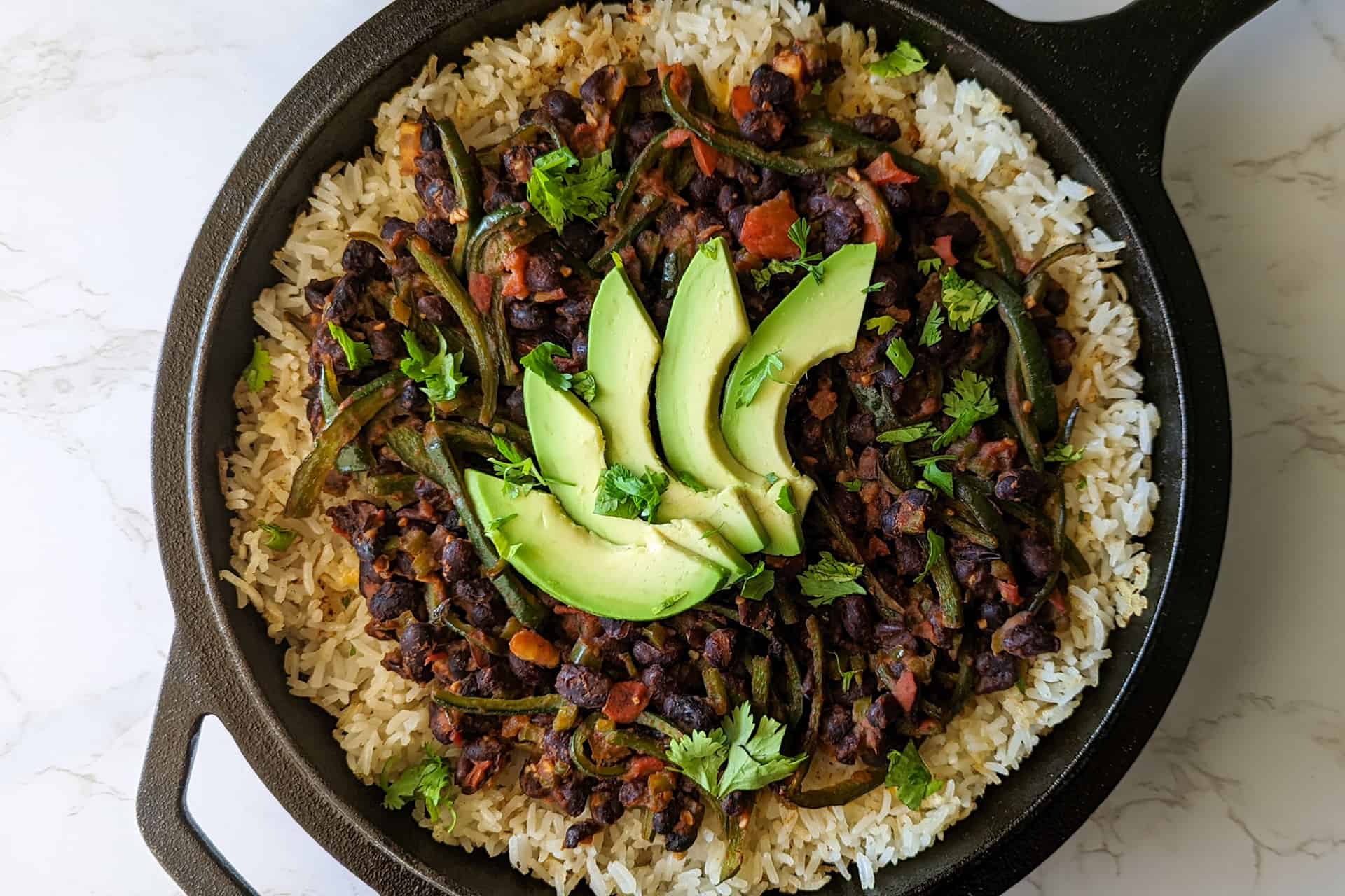 A black bean and rice bake in a cast iron skillet topped with sliced avocado