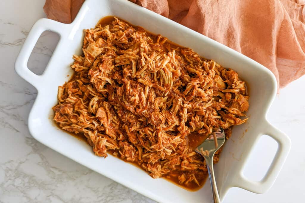 A serving dish of shredded chicken tinga with a fork