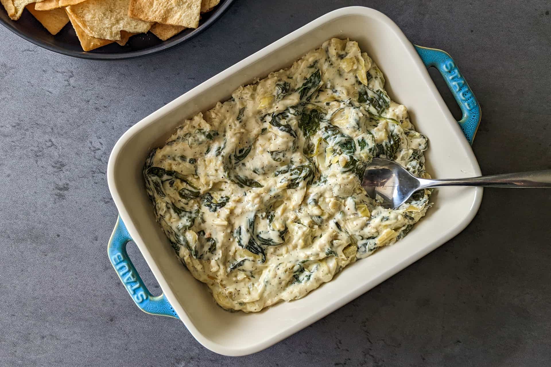 A casserole dish of cheesy spinach and artichoke dip with pita chips