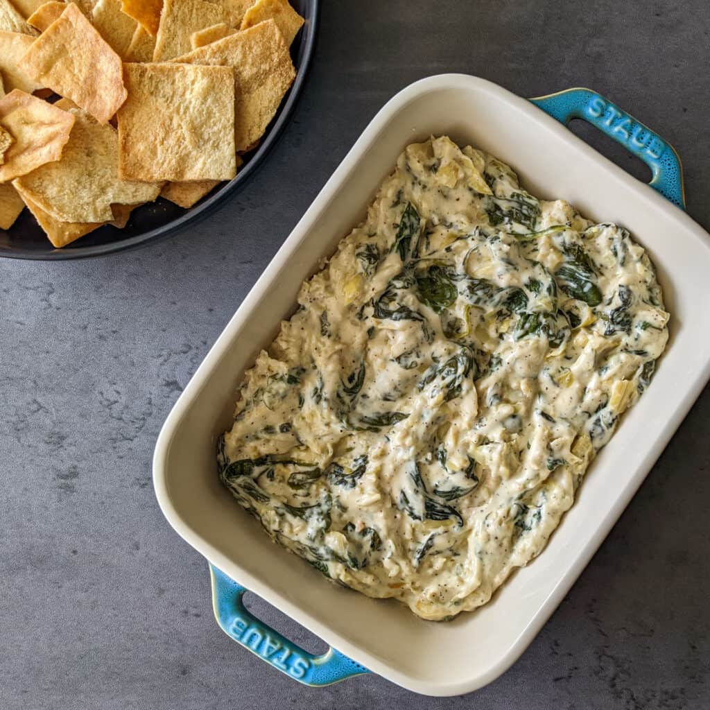 A dish of cheesy spinach and artichoke dip with pita chips