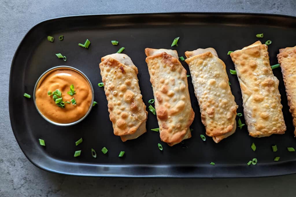 A plate of crispy cheeseburger egg rolls with sriracha mayo dipping sauce