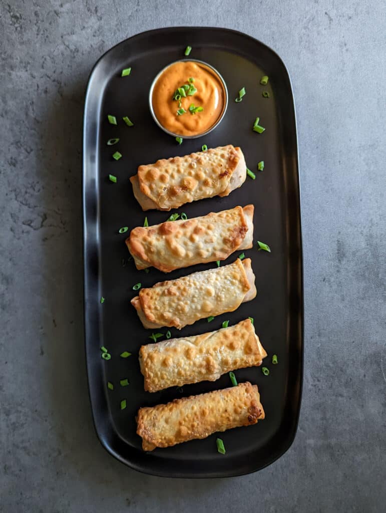 A plate of crispy cheeseburger egg rolls served with spicy mayo dipping sauce