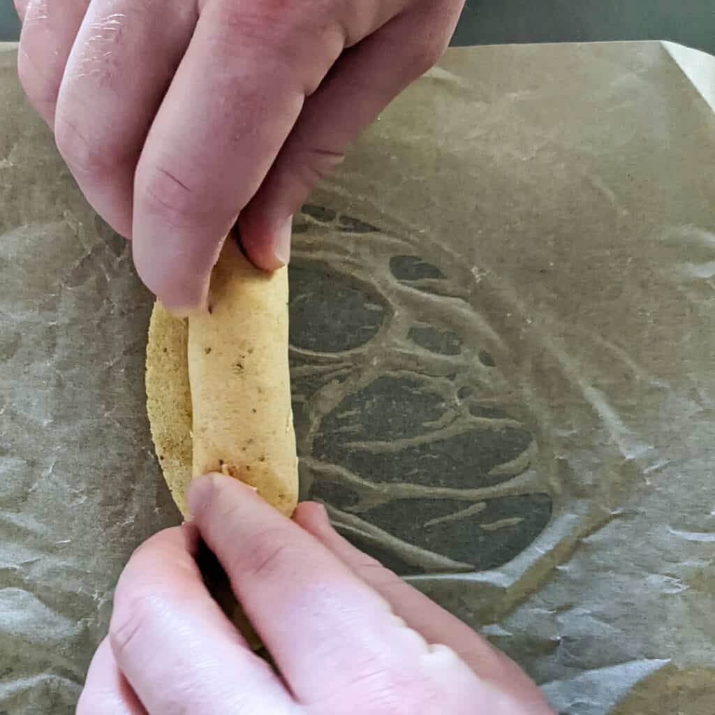 Rolling a corn tortilla into the shape of a taquito