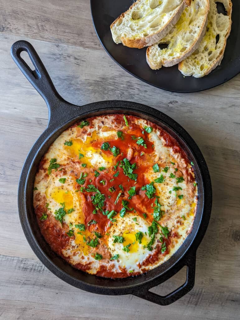 A cast iron skillet of shakshuka served with a plate of toasted bread
