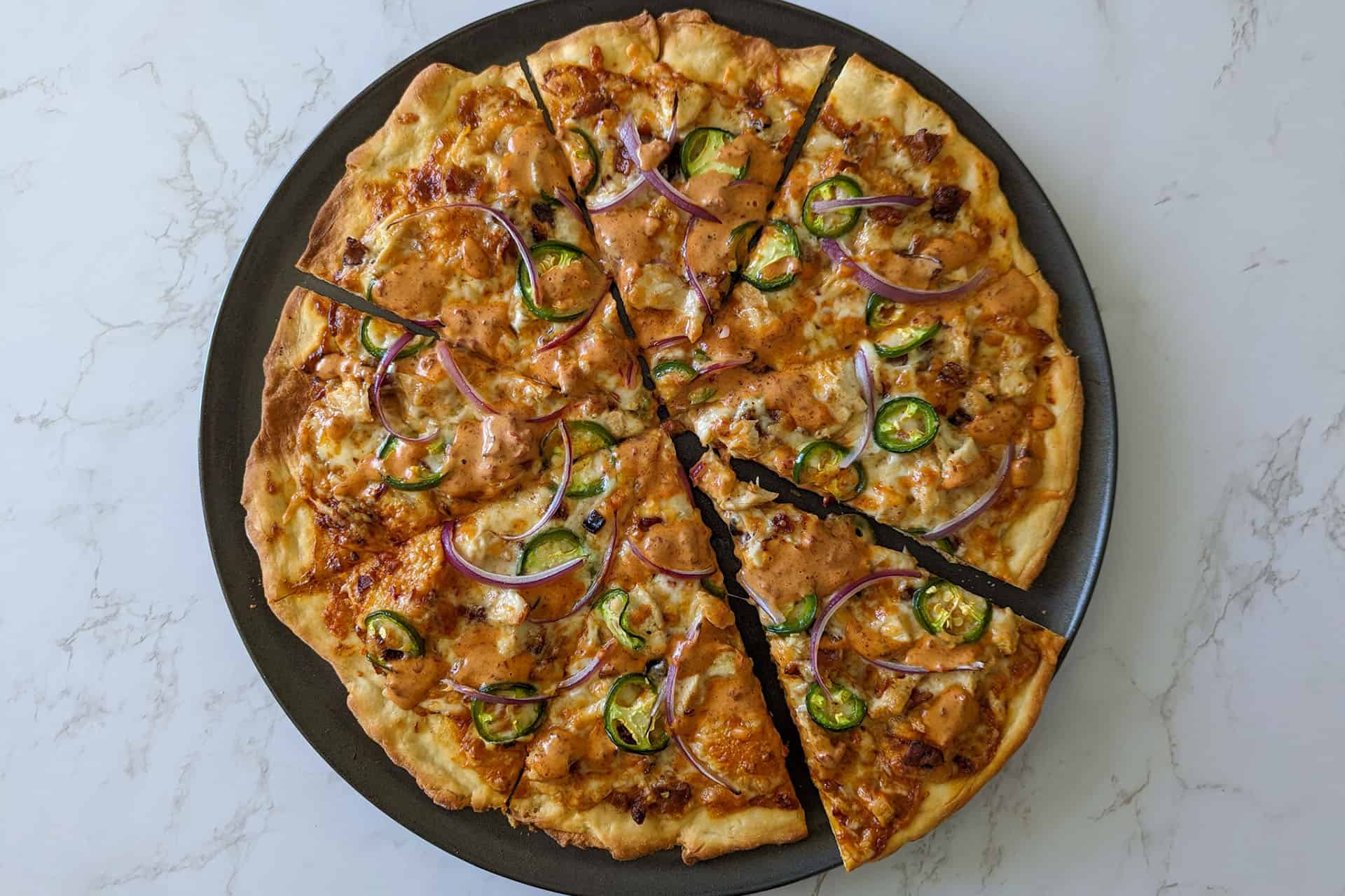 Spicy chicken bacon ranchero pizza topped with jalapenos and red onions