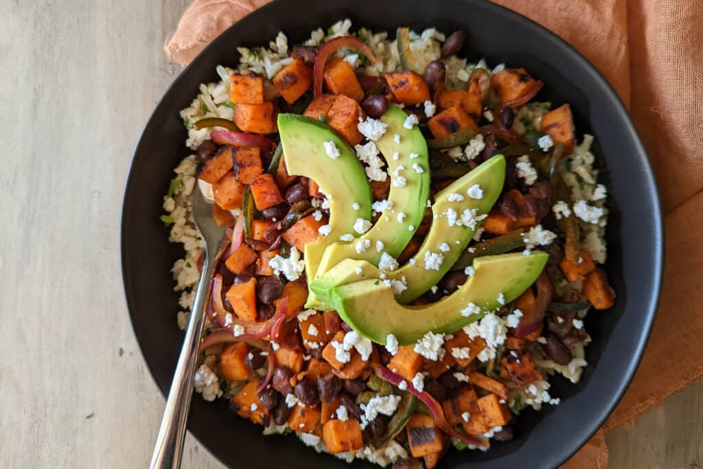 A healthy power bowl with brown rice, black beans, sweet potato, peppers, onion, and avocado