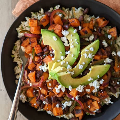 A healthy power bowl with brown rice, black beans, sweet potato, peppers, onion, and avocado