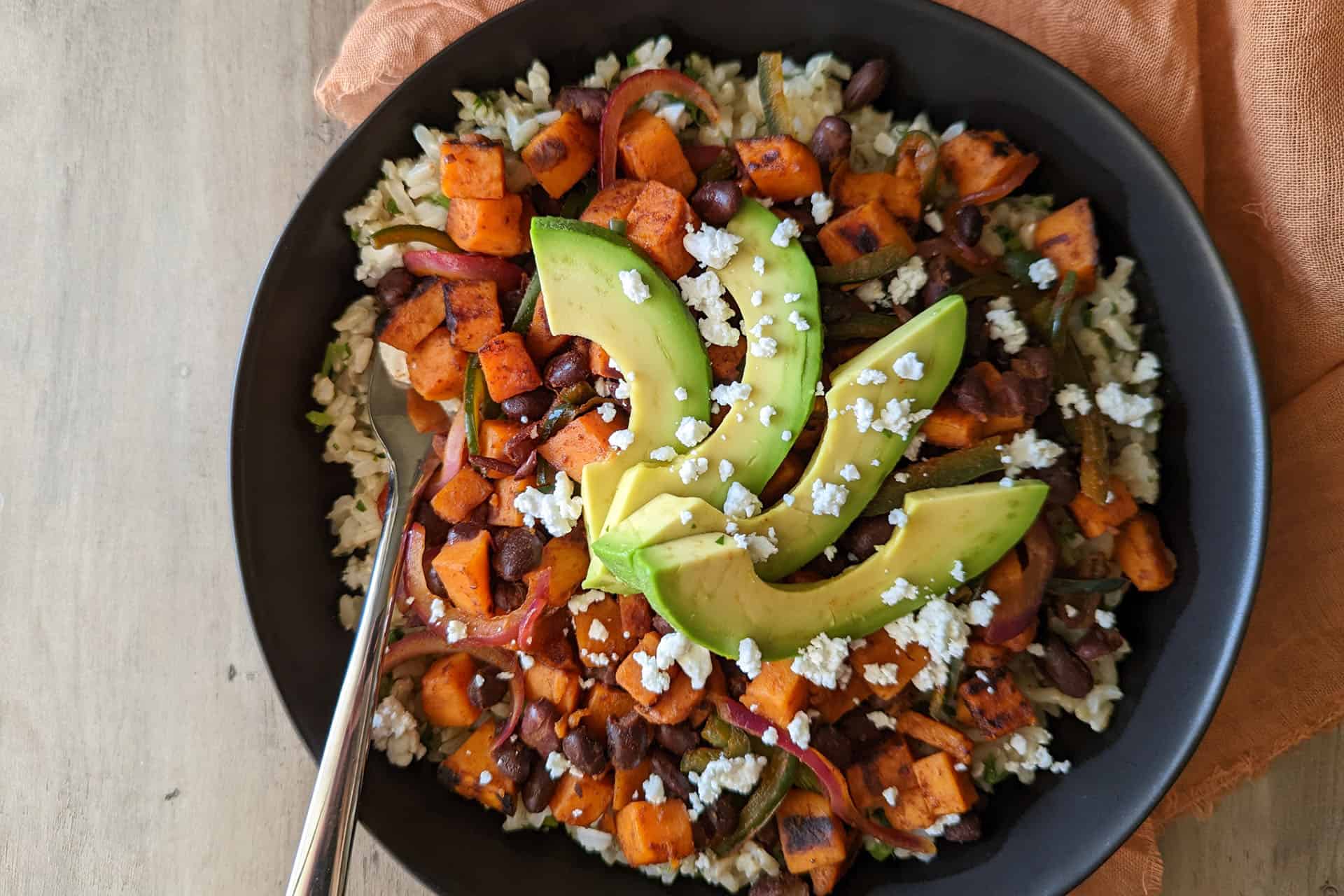 A healthy power bowl with brown rice, black beans, sweet potato, peppers, onion, and avocado