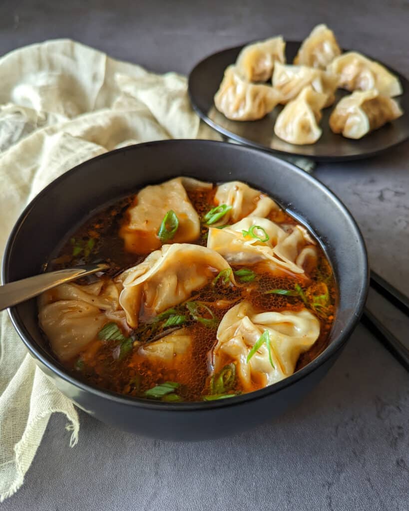 Spicy szechuan wonton soup with a plate of pork dumplings in the background