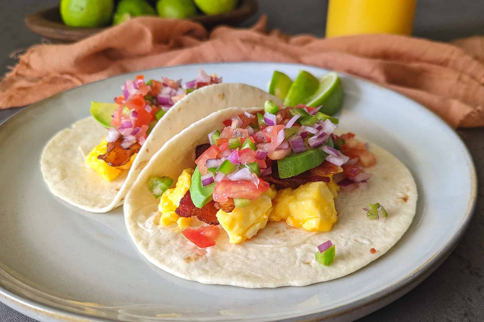 Two breakfast tacos filled with eggs, bacon, avocado, and pico de gallo