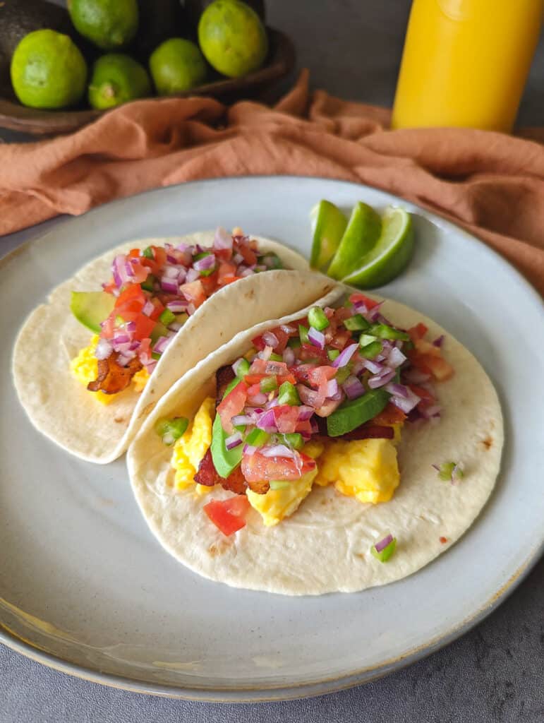 A plate of breakfast tacos served with lime wedges and orange juice