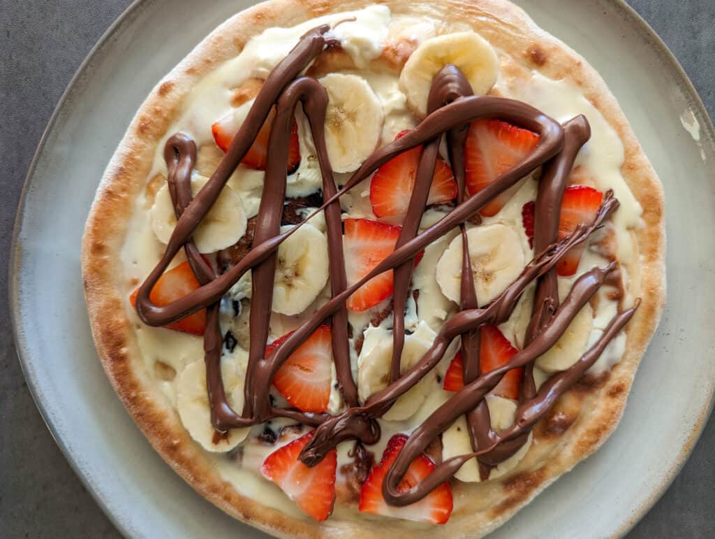 Dessert pizza with strawberry and banana slices, mascarpone cheese, and nutella
