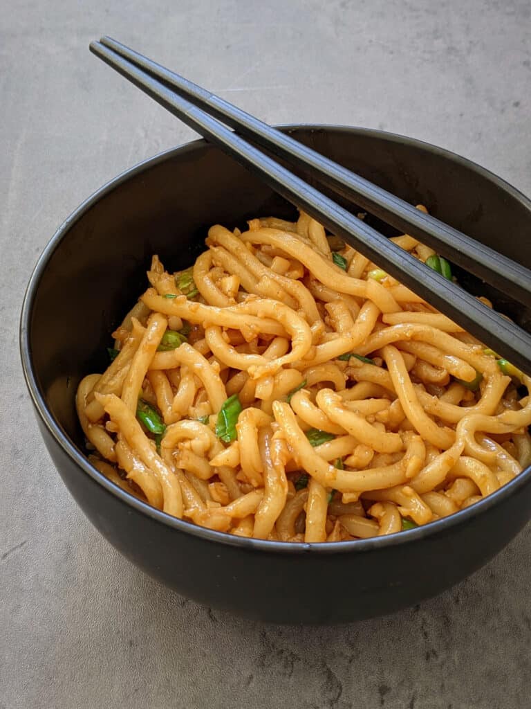 Asian garlic noodles served in a black bowl with a pair of chopsticks