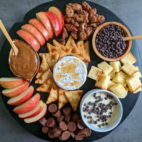 A sweet charcuterie board with apples, caramel, crackers, brie, mascarpone, brioche, candied nuts, and chocolates