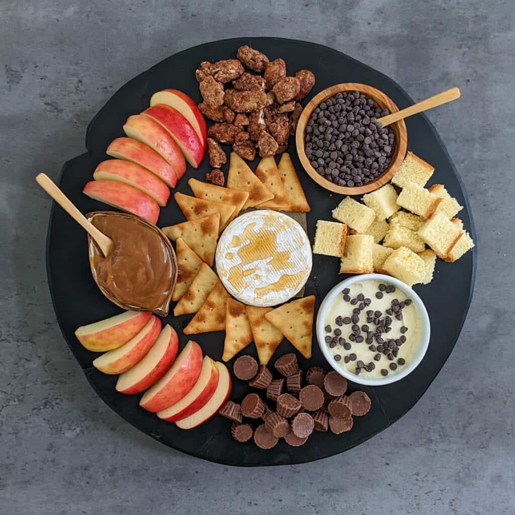A sweet charcuterie spread idea with chocolates, candied nuts, sweet cheeses, apples, and caramel