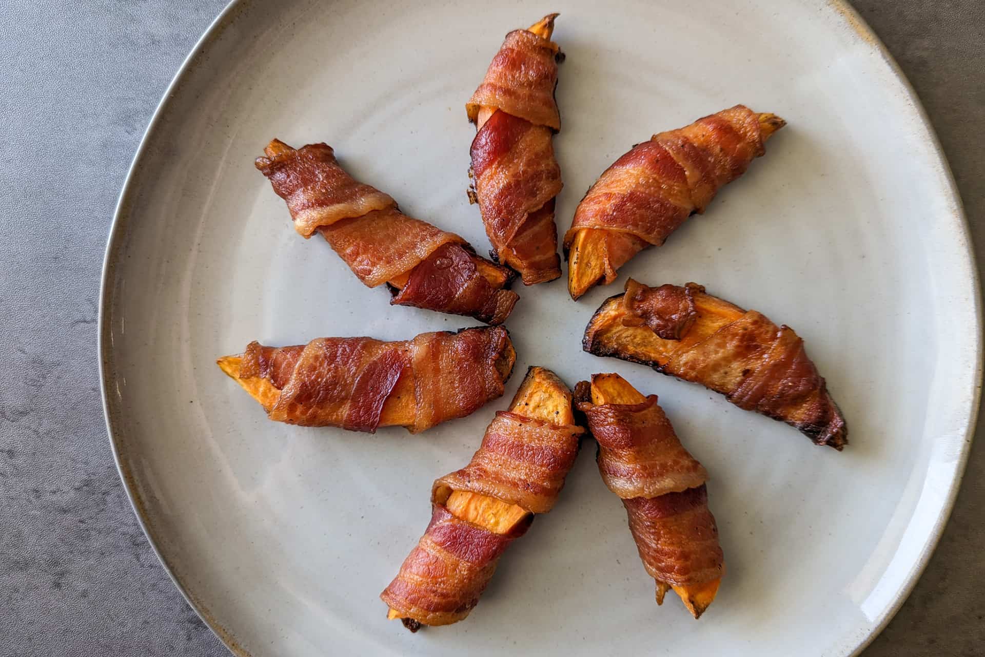 Bacon wrapped sweet potato wedges served on a large plate