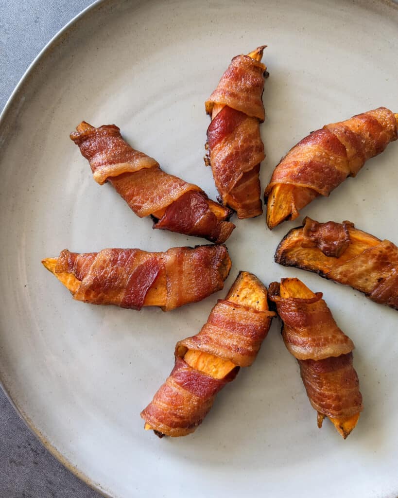 Crispy bacon wrapped sweet potato wedges fanned out on a plate