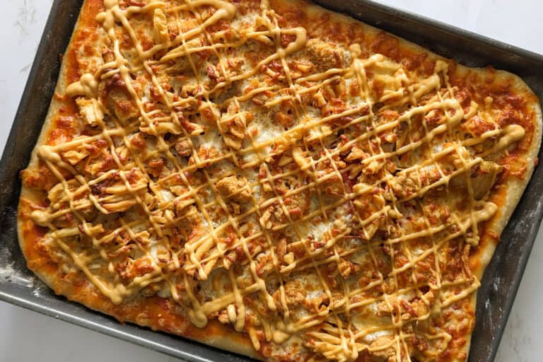 Homemade sheet pan chick-fil-a pizza topped with chicken and fries and drizzled with sauce