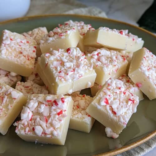 A plate of white chocolate peppermint fudge topped with crushed candy canes and sliced into cubes