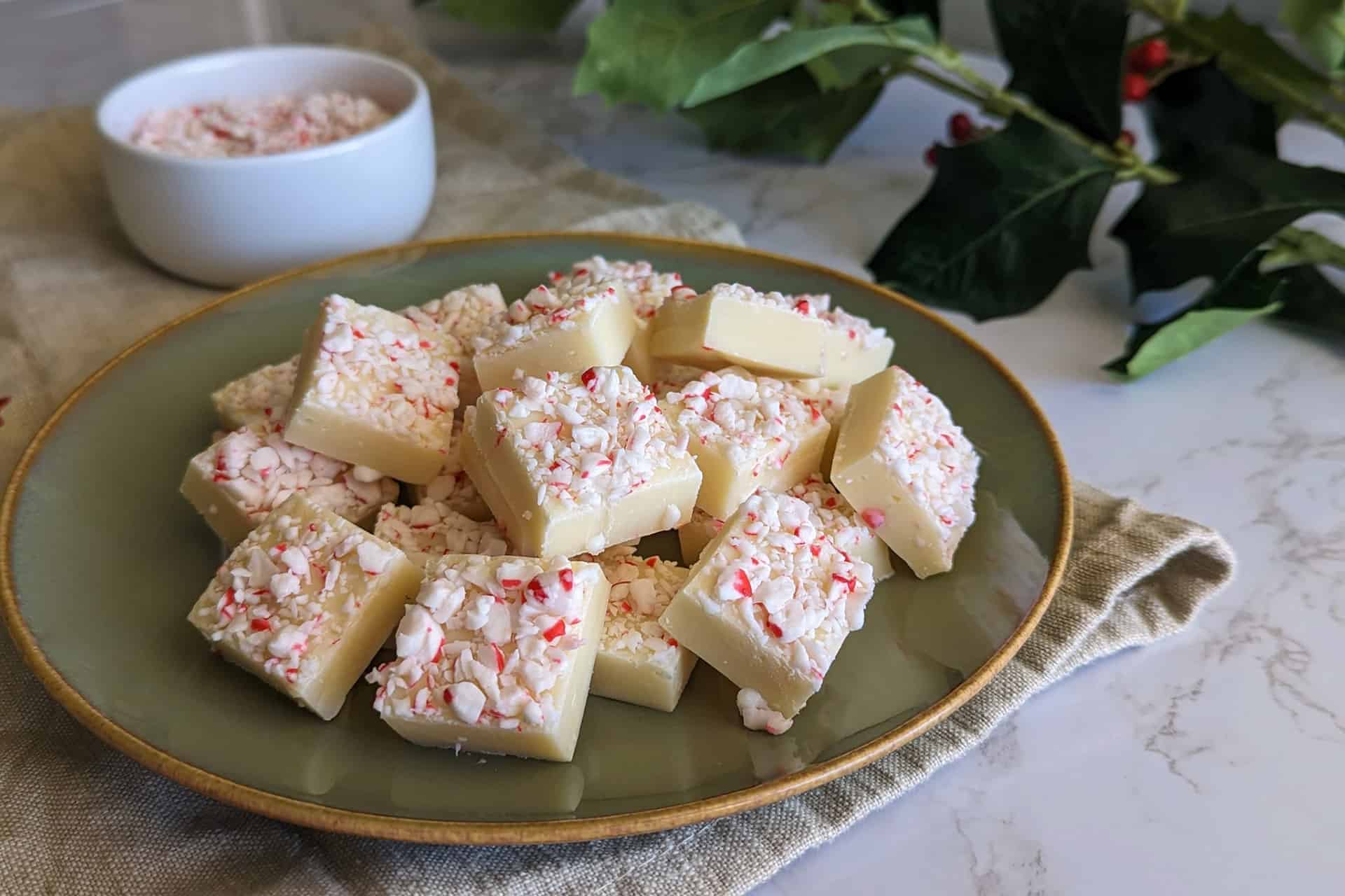 White chocolate peppermint fudge cubes on a plate with a branch of holly in the background