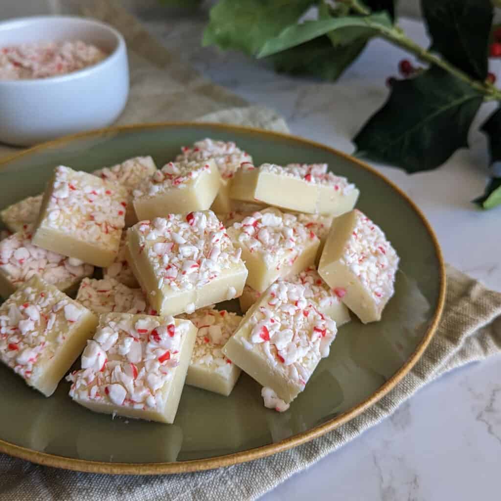 White chocolate and mint fudge topped with crushed candy canes, sliced into cubes and served on a plate