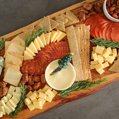 A Christmas charcuterie board with meats, cheeses, crackers, nuts, and fresh rosemary sprigs