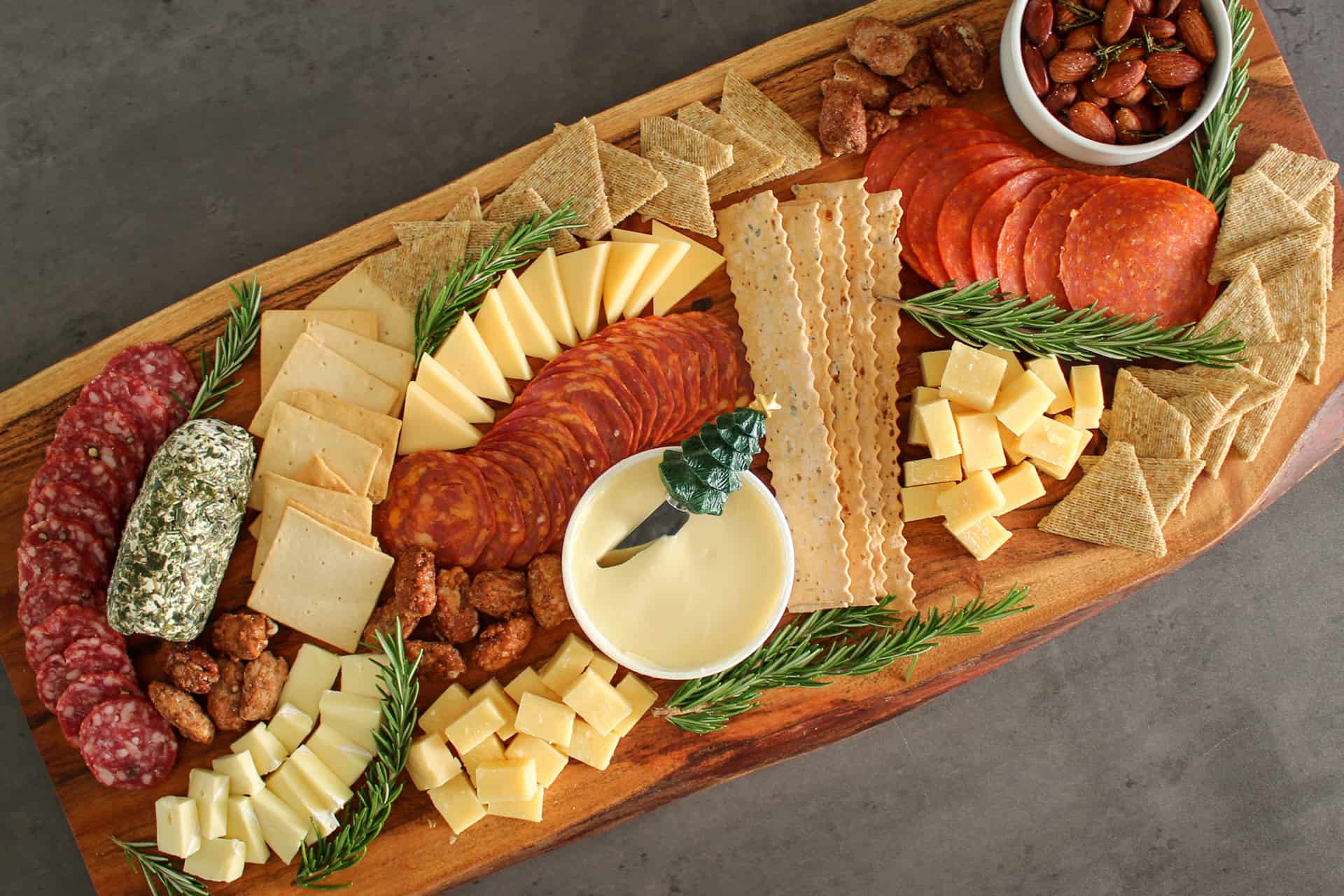 A Christmas charcuterie board with meats, cheeses, crackers, nuts, and fresh rosemary sprigs