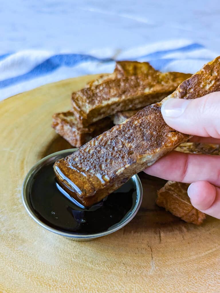 A french toast stick being dipped in maple syrup