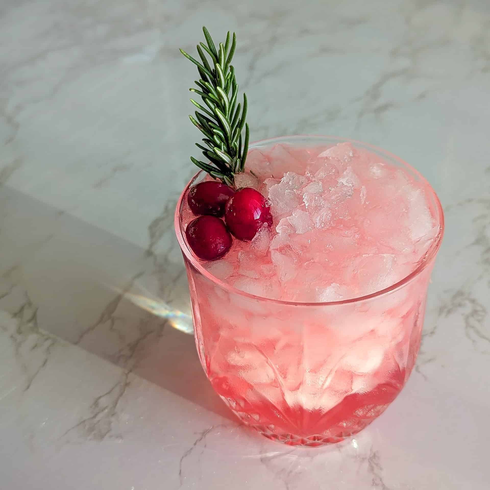 A Christmas cocktail made with vodka and cranberry juice in a crystal glass, garnished with a rosemary sprig and frozen cranberries