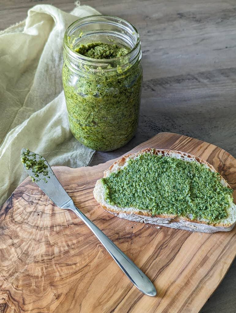 A jar of homemade nut free pesto with some spread on a slice of Italian bread