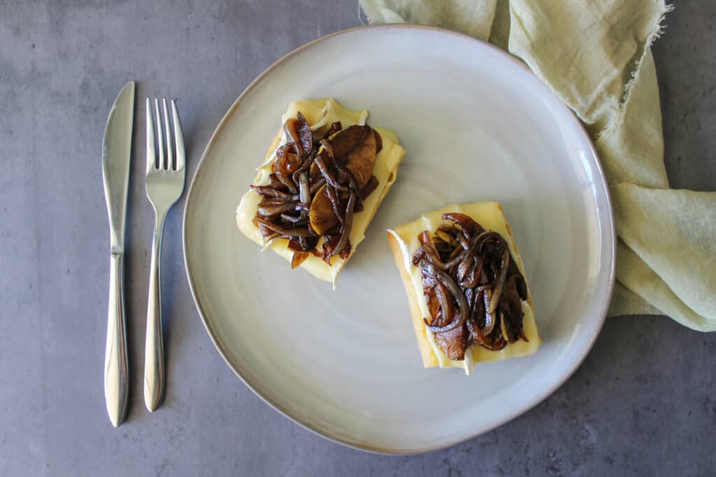 Balsamic glaze caramelized onions and apples on an open faced brie sandwich with a fork and knife