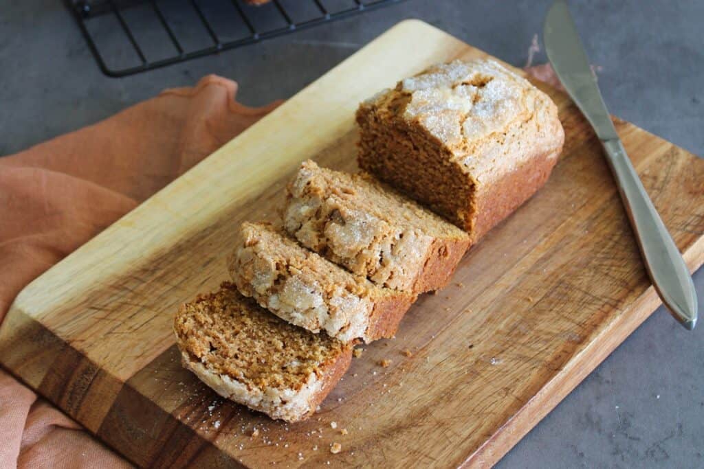 A loaf of sweet potato quick bread with a few pieces sliced on a cutting board