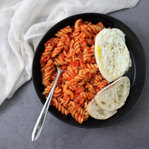 Shakshuka pasta dinner with a fried egg and bread in a bowl