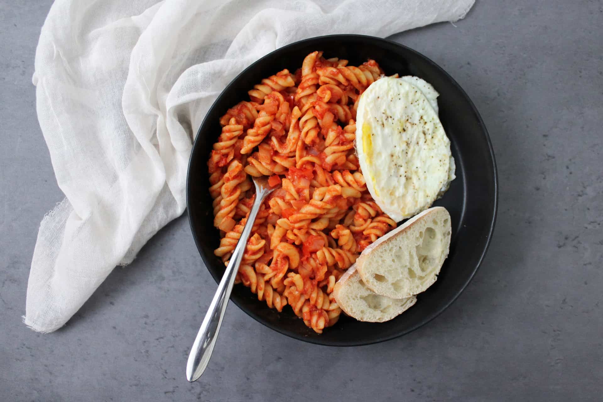 Shakshuka pasta dinner with a fried egg and bread in a bowl