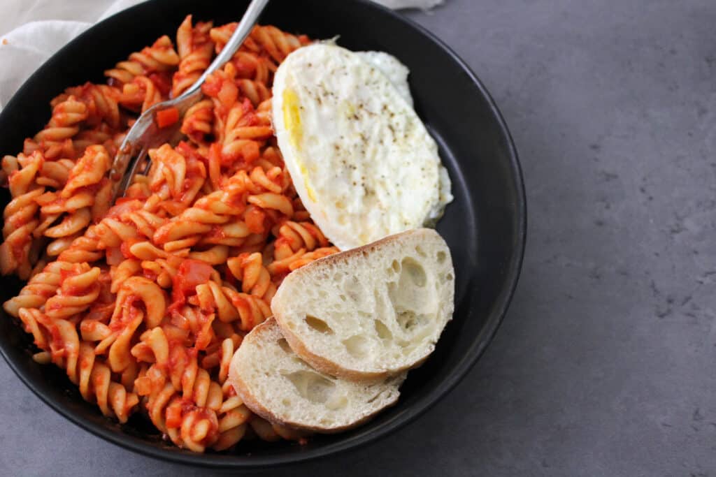 A bowl of shakshuka pasta with a fried egg and some fresh bread