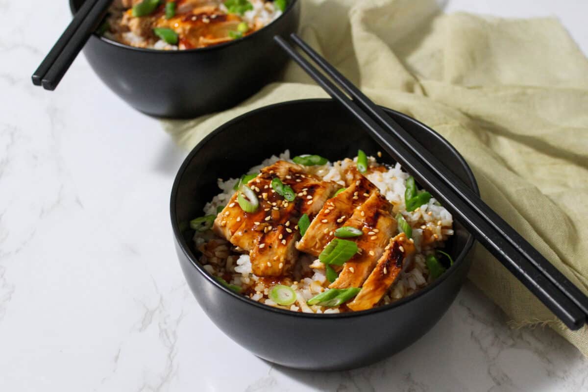Two bowls of takeout style teriyaki chicken on white rice with sesame seeds and scallions