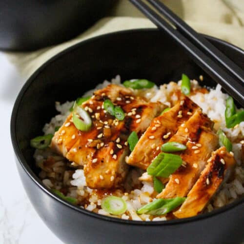 A bowl of rice with teriyaki grilled chicken, toasted sesame seeds, and scallions