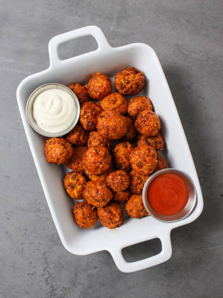 A dish of healthy air fryer buffalo cauliflower bites served with ranch and hot sauce