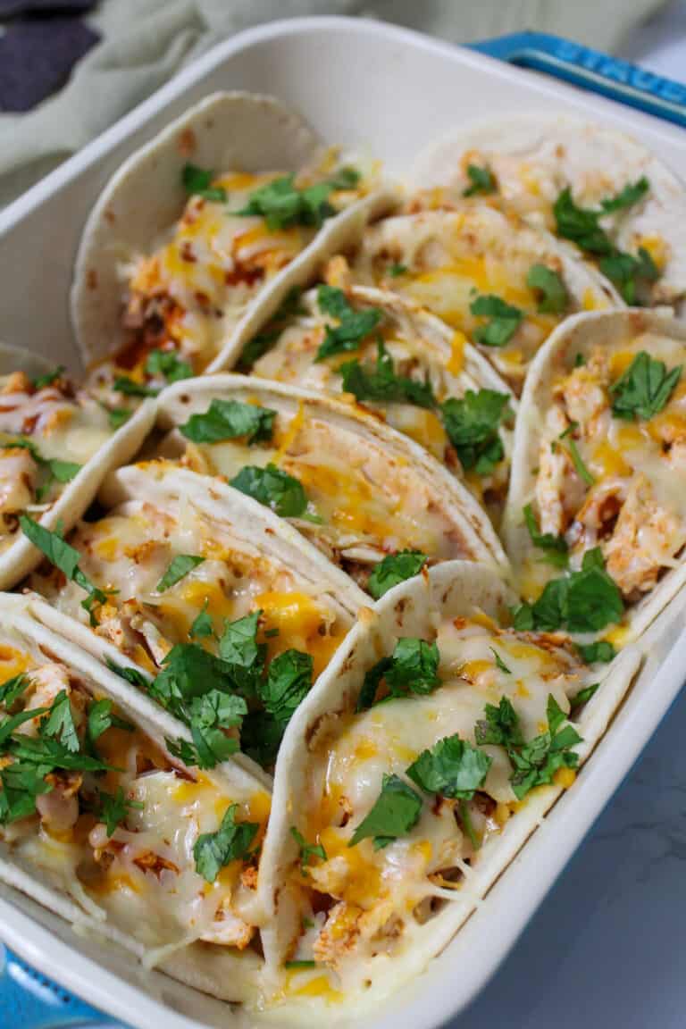 A dish of baked chicken tacos made with flour tortillas, shredded chicken, and cheese