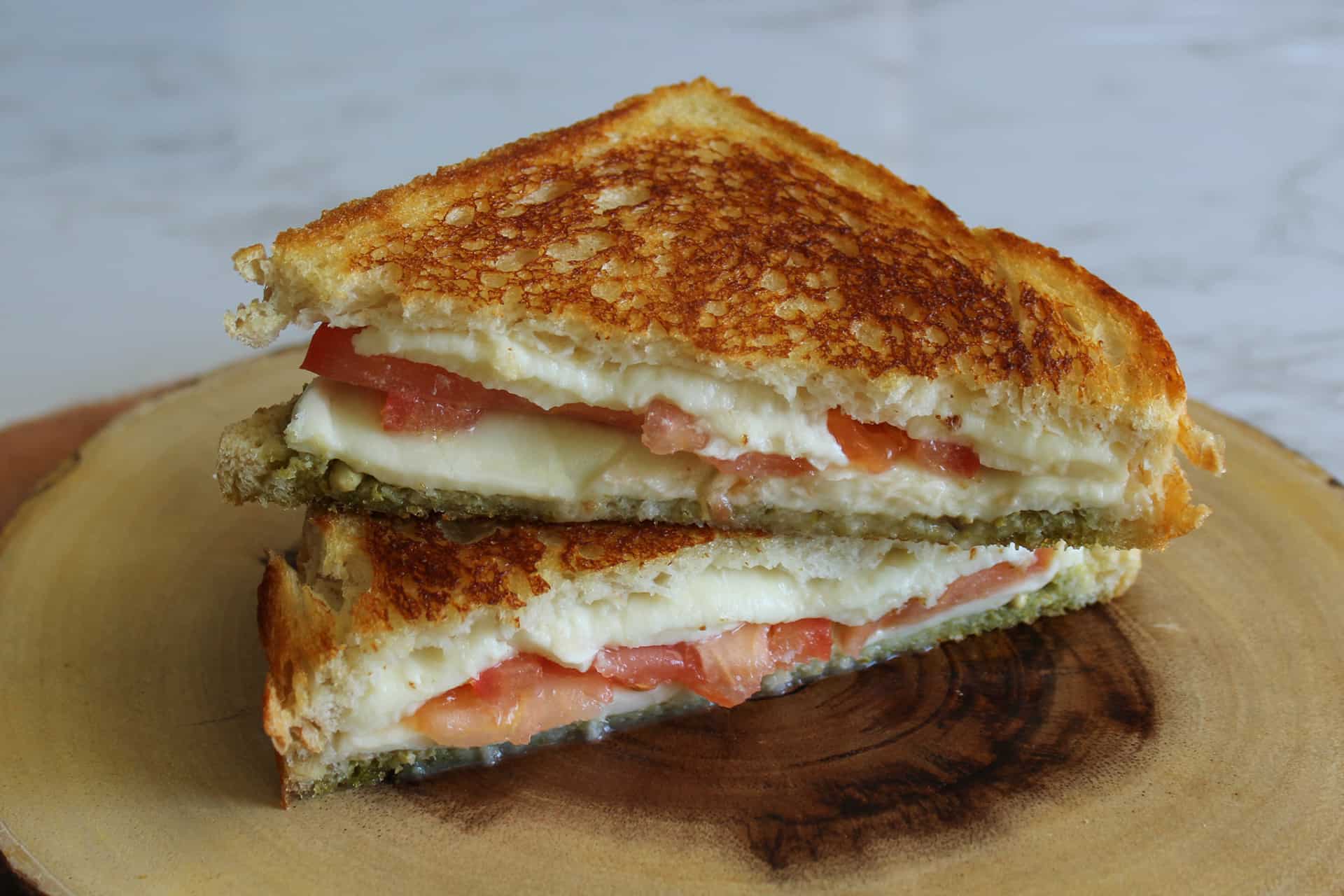 Two halves of a caprese panini with tomato, mozzarella, and pesto stacked on a plate